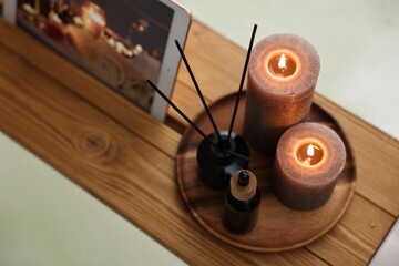 Wooden tray with tablet, burning candles and aroma products on bathtub, above view
