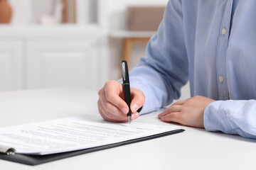 Woman signing document at white table indoors, closeup. Space for text
