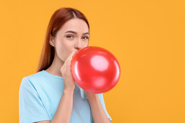 Woman inflating red balloon on orange background, space for text