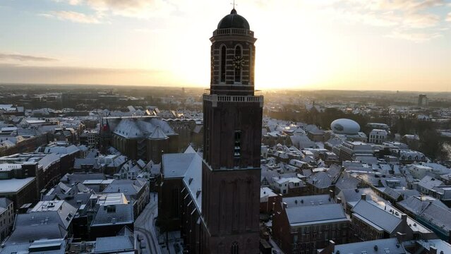 Zwolle Peperbus church tower rising up over the snow covered rooftops in the downtown district aerial drone view during a cold winter sunrise.