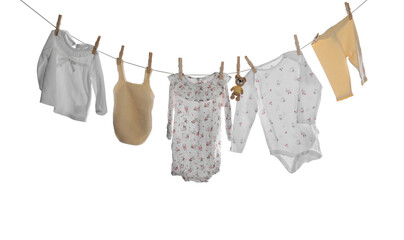 Different baby clothes and toy bear drying on laundry line against white background