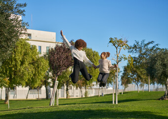 Obraz premium two sisters with curly afro hair have fun playing jumping on the grass in a city park on a sunny day