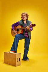 Full length portrait of charismatic elderly woman singing while playing guitar dressed denim...