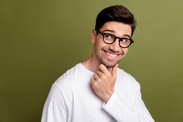 Portrait of handsome guy wearing white pullover touching chin and classic eyeglasses looking empty space isolated on khaki color background