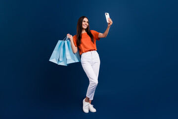 Full length photo of sweet shiny lady wear orange t-shirt holding bargains recording video vlog device isolated dark blue color background