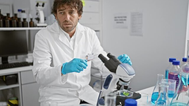 A focused man in a lab coat examining specimens under a microscope in a modern laboratory setup.