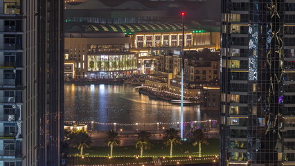 Fototapeta premium Aerial view of Dubai Fountain in downtown with palms in park next to shopping mall and souq day to night timelapse, UAE
