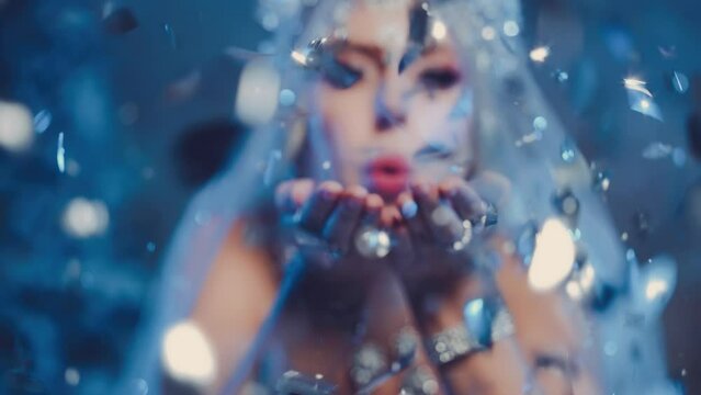 Art portrait Fantasy woman snow queen blows on shining sparkles glitter creating magic cold in forest, white dress crown icicles. Fairy tale girl frozen princess lady Winter nature trees ice blue fog
