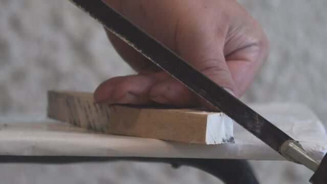 A man saws a wooden billet or part with a hacksaw on metal