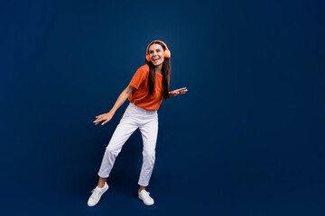 Fototapeta na wymiar Full length photo of cute sweet lady wear orange t-shirt headphones dancing discotheque empty space isolated dark blue color background