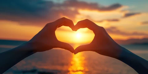 Foto op Canvas A close-up of hands forming a heart shape with a beautiful sunset in the background - love and togetherness concept Ideal for romantic themes and greeting cards © kimly