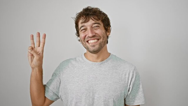 Confident young man, pointing up showing number three with fingers, happy smile brightening up his casual t-shirt look on white isolated background.