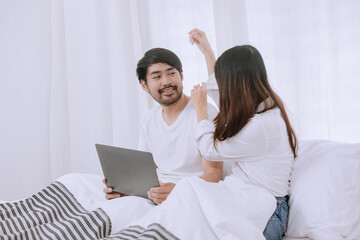Fototapeta premium Happy asian man and woman using laptop sitting relaxed on a bed at home enjoy, Happy lover hug each other and smiling on the bed, Male and female couple concept.