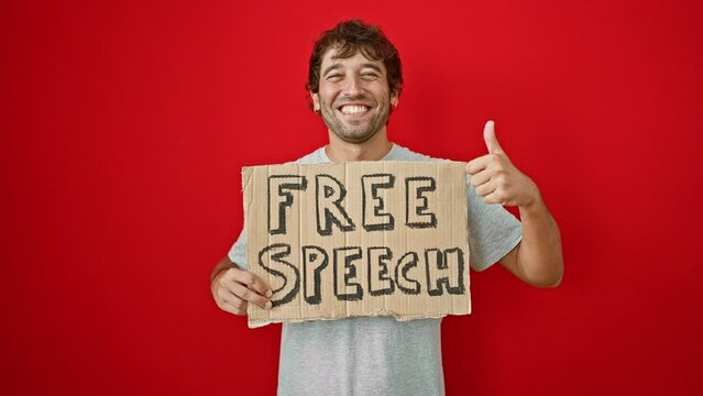 Cheerful young man flaunting his 'free speech' banner, giving the thumbs-up sign of approval! cool guy with a confident smile isolated against a vibrant red wall.
