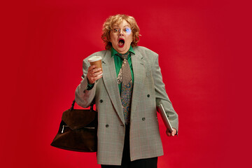 Portrait of excited, shocked mature woman, pensioner dressed smart casual outfit against red studio background. Concept of business, fashionable older adults, active seniors in modern life