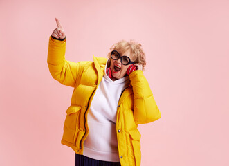 Portrait of overjoyed mature woman wearing warm winter yellow coat and listening music in...