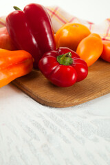 Cutting board with assort of different tomatoes and bell pepper on white wooden background..