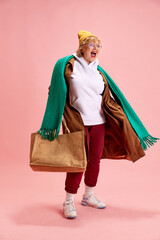 Driven, cheerful elderly woman in fashionable winter outfit rejoices after shopping with large...