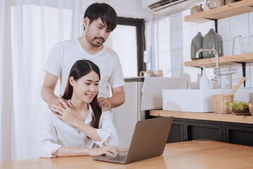 Happy love Asian young man and woman using laptop together in the kitchen relaxing at home.