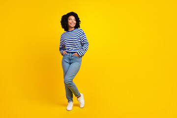 Fototapeta na wymiar Full length photo of cute girl with chevelure wear pullover arms in pockets look at offer empty space isolated on yellow color background