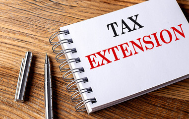 TAX EXTENSION text on notebook with pen on wooden background