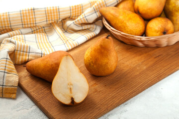 Cutting board with whole and halves pears, wicker basket and yellow kitchen towel on white wooden background..