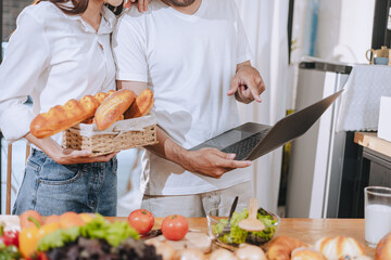 Happy love Asian young man and woman cooking food together in the kitchen relaxing at home.