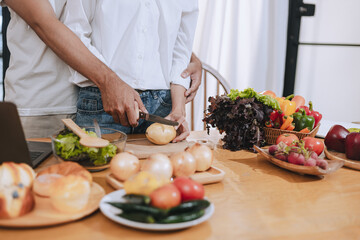 Happy love Asian young man and woman cooking food together in the kitchen relaxing at home.