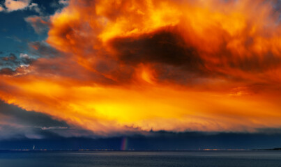A very bright large colored storm cloud with a rainbow on the background of a narrow strip of the city on the horizon