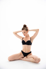 Girl in black underwear sits and poses on a white background