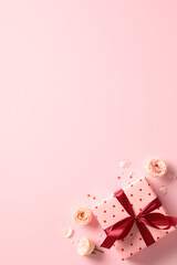 Valentine's day pink gift box with red ribbon bow, roses buds, confetti on pastel pink background. Flat lay, top view.