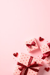 Happy Valentine's Day concept. Flat lay composition with pink gift boxes with red ribbon bow, red hearts on pastel pink background. Top view.