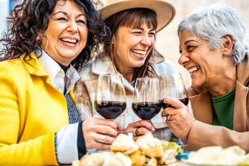 Happy senior women drinking red wine at bar restaurant - Mature people having fun hanging out on city street - Life style concept with older friends smiling and laughing together	
