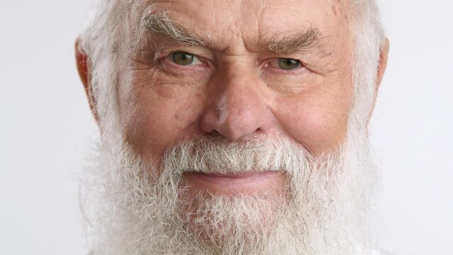 An elderly man with a full white beard playfully winking one eye and smiling, set against a clean white background, showcasing a spirited and jovial character. Camera 8K RAW. 