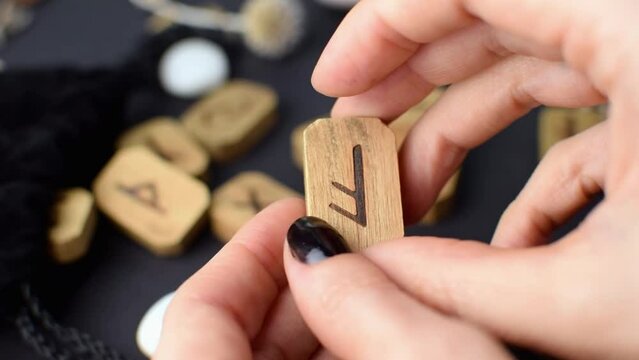 Scandinavian wooden runes in the hands of a fortune teller on a black table with velvet bags and stones. Magic esoteric symbols and signs for divination and prediction of the future and fate.