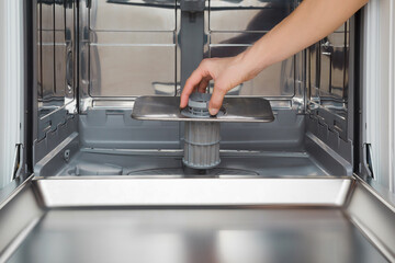 Young adult woman hand holding and putting clean filter in dishwasher. Closeup. Front view.