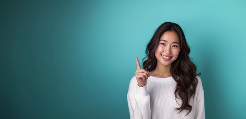 Asian woman presents, pointing finger up with copy space blue background, portrait beauty, confidence, and elegance of a young and attractive Asian model.