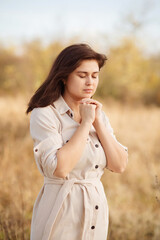 portrait of young woman praying on nature, girl thanks God with her hands folded under chin,...