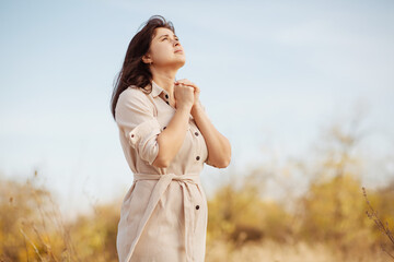 portrait of young woman praying on nature, girl thanks God with her hands folded under chin,...