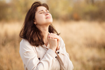 portrait of young woman praying on nature, girl thanks God with her hands folded under chin, concept of religion