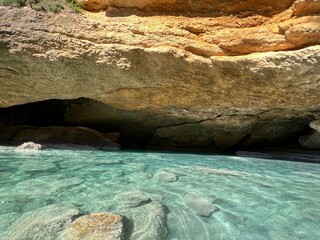 Blue sea water on pebbles beach on rocky coast.