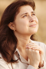 close up face of young woman praying on nature, girl thanks God with her hands folded under chin, concept of religion