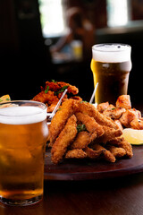 portion of seafood with breaded fish and shrimp and grilled salmon with french fries and two glasses of craft beer blurred background