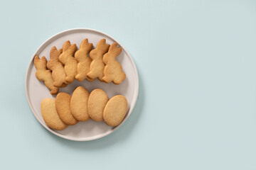 Easter homemade cookies shaped of eggs and bunny in white plate on blue background. View from above. Festive food and kids snacks. Greeting card with copy space.