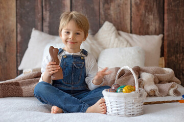 Sweet preschool boy in studio, playing with, egg for Easter and eating chocolate, child on Easter...