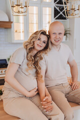  Smiling couple in kitchen, pregnant woman leaning on man, both in beige outfits, exuding warmth and love