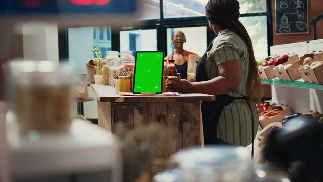 Digital layout of greenscreen on tablet placed in farmers market, display showing blank copyspace screen next to women talking about additives free bulk items. Isolated mockup template. Tripod shot.
