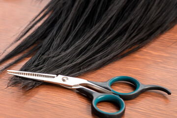 hairdresser's work. a black strand of long hair with scissors lies on a wooden table, close-up view