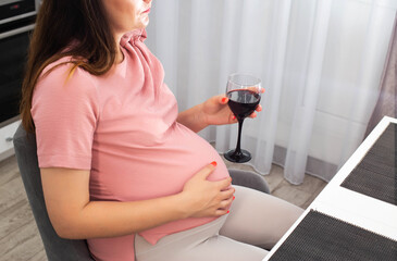 A pregnant girl with a big belly in a pink blouse holds a glass of wine. The concept of drinking...