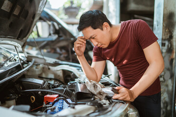 a young male mechanic is confused while working on a machine in a repair shop